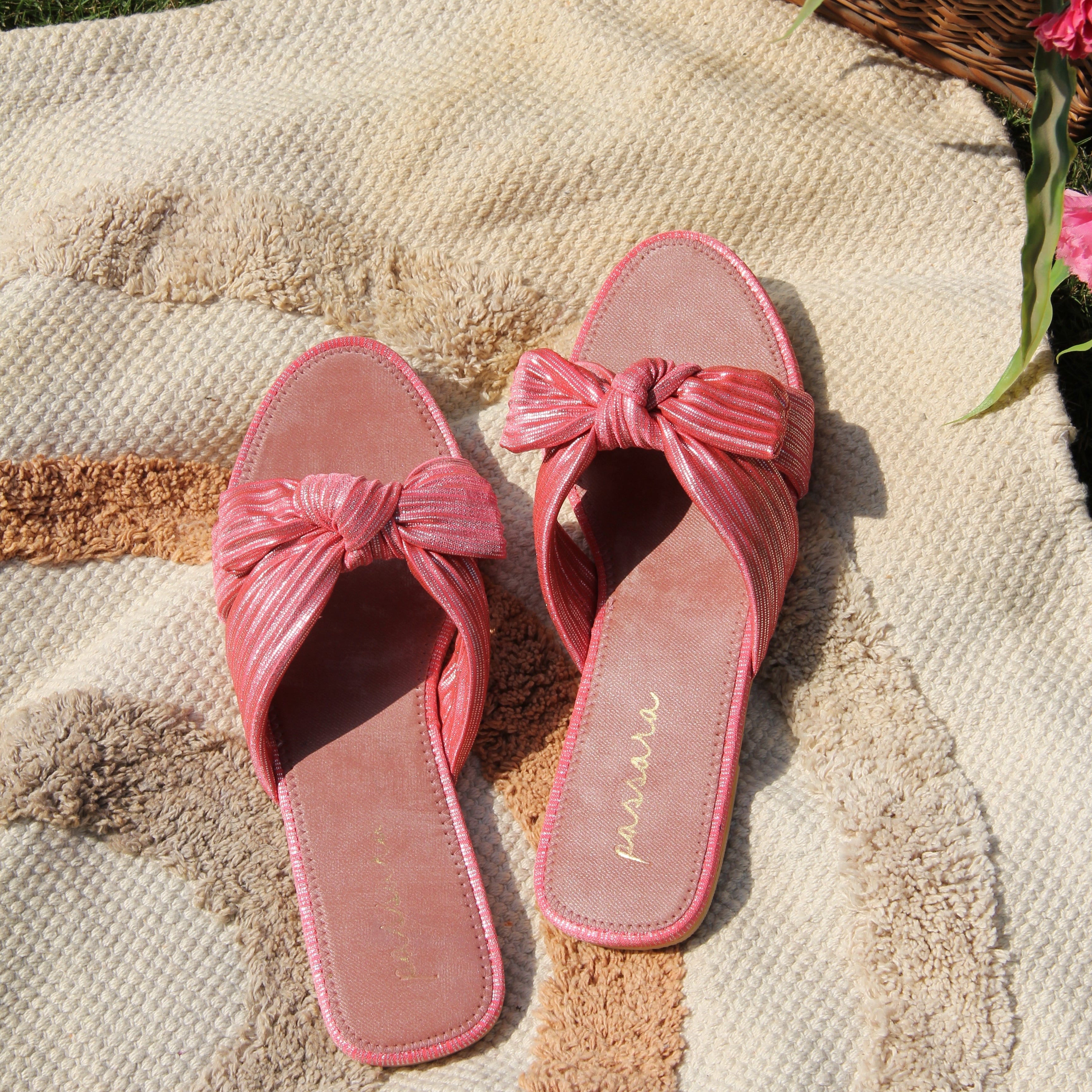 Pink sandals with a bow on a textured surface with flowers in the background