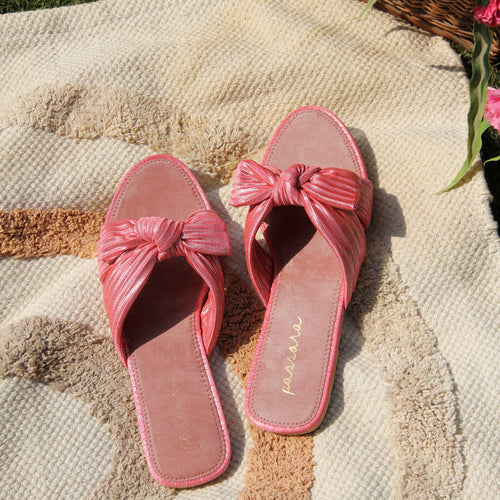 Pink sandals with a bow on a textured surface with flowers in the background
