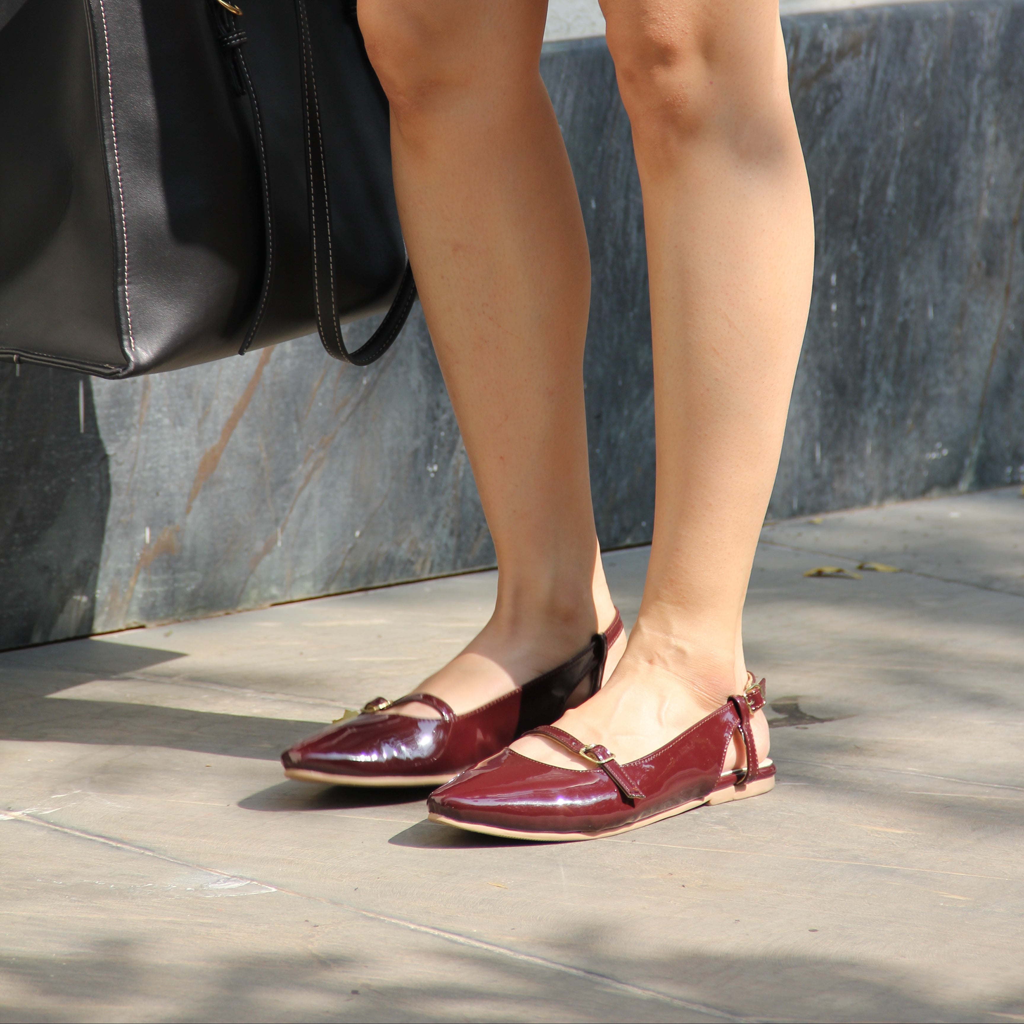 Person wearing red high heels stepping onto a curb with a black bag and briefcase.