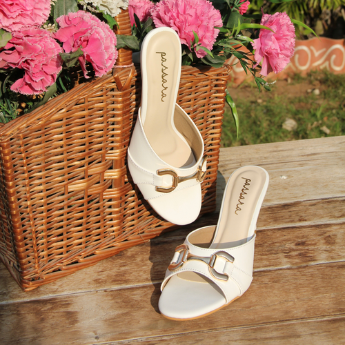 White sandals with gold buckles next to a basket of pink and white flowers on a wooden surface.