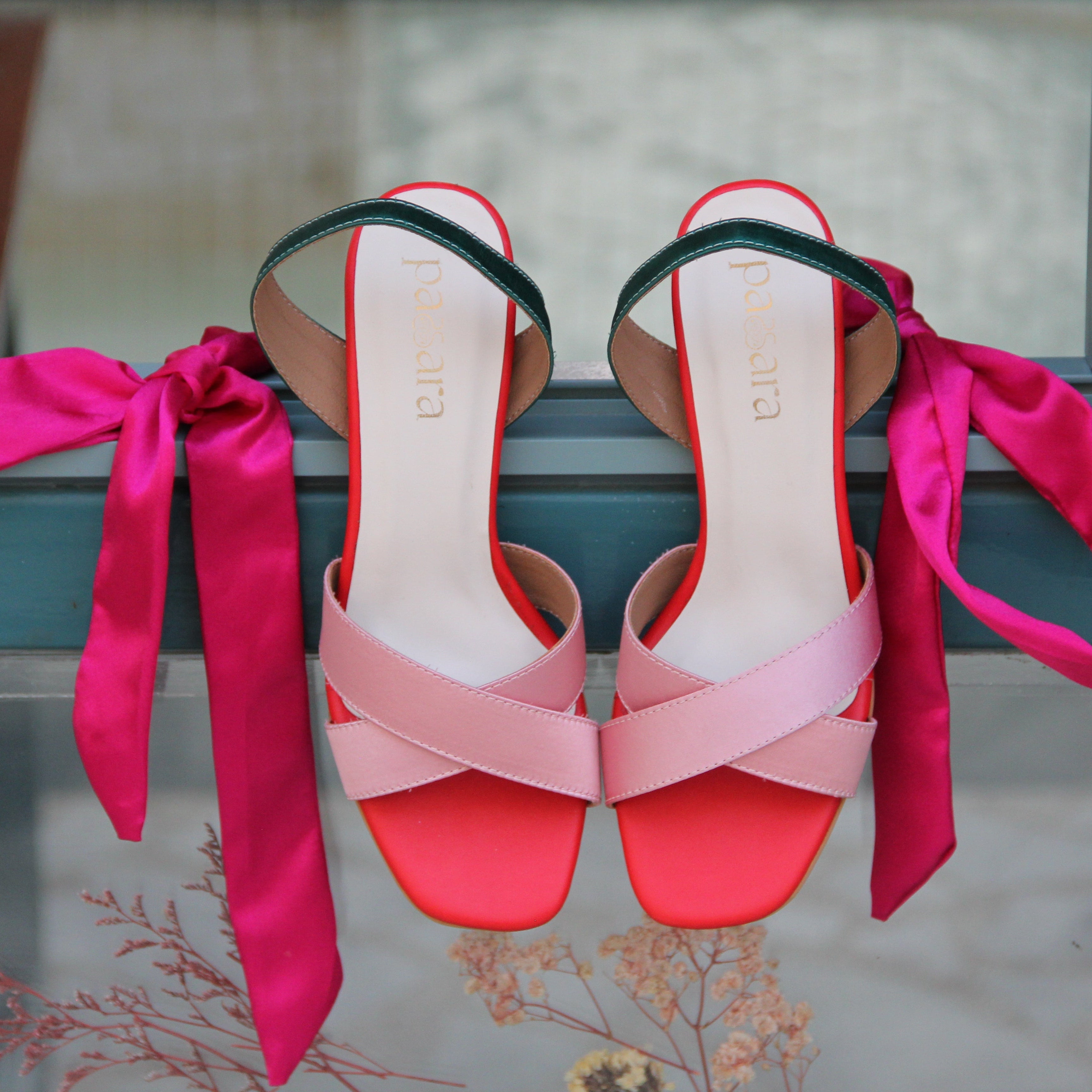 Pair of pink and red high-heeled shoes with ribbons on a metal surface.