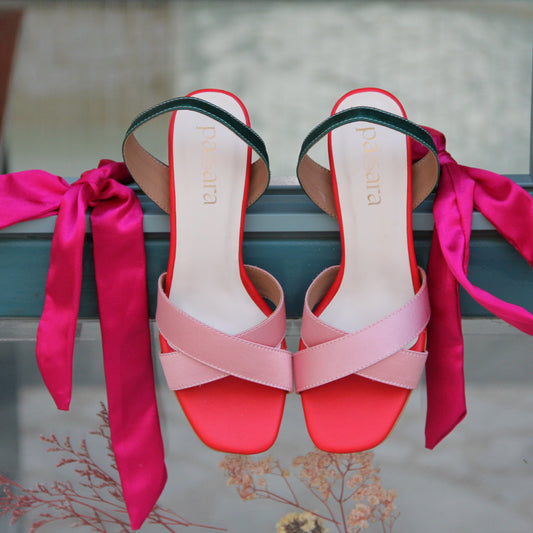 Pair of pink and red high-heeled shoes with ribbons on a metal surface.