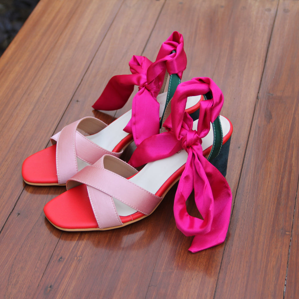 Pair of red and pink high-heeled shoes with ribbons on a wooden surface