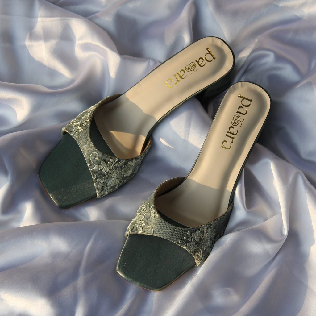 Pair of high-heeled shoes with glittery green cap-toe on a textured fabric background