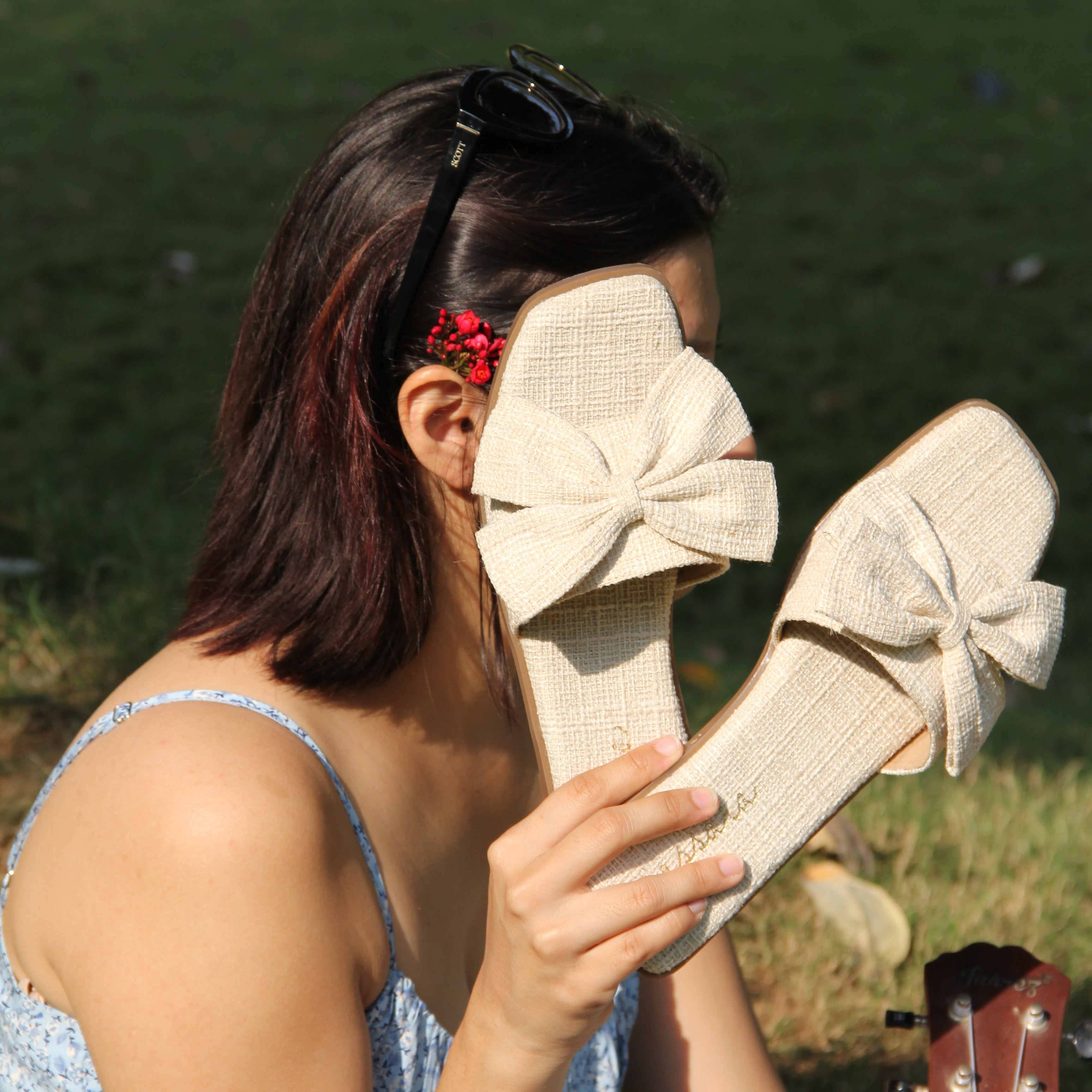Person holding a beige shoe with a large bow, standing on grass