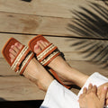 Brown sandals with striped straps on a wooden floor