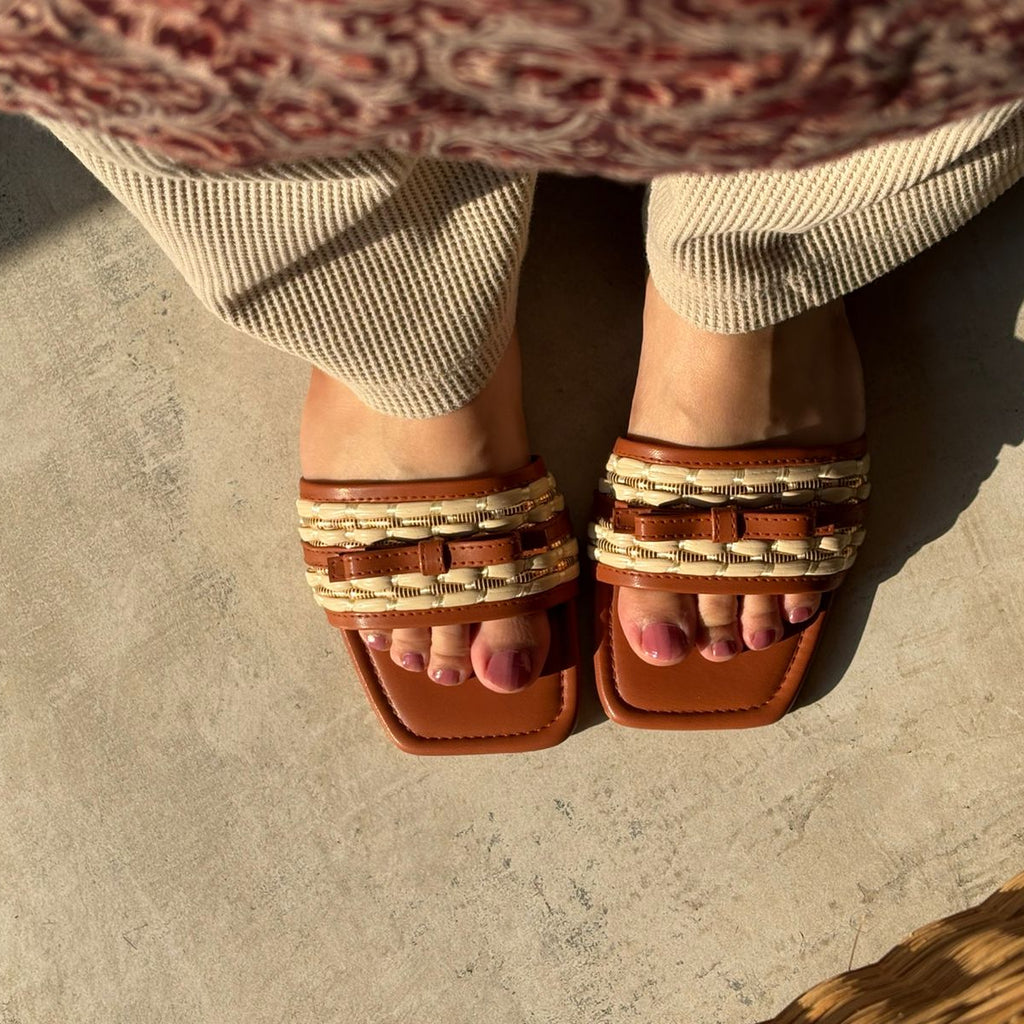 Brown sandals with decorative straps worn by a person on a stone surface