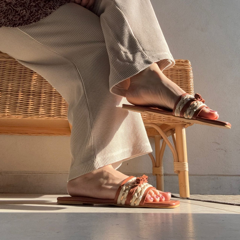 Person wearing pink sandals with floral straps sitting on a wicker chair.