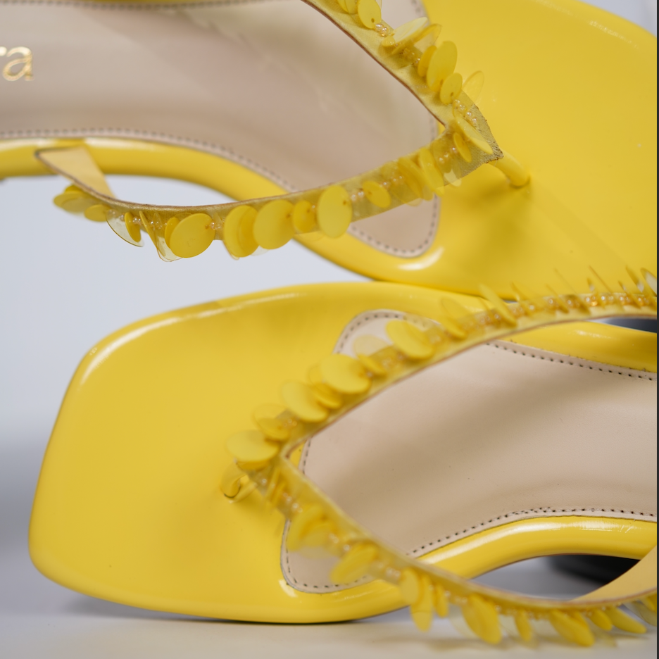Yellow high-heeled shoes with decorative elements on a light gray background