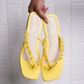 Yellow shoes with decorative straps held by a hand against a light gray background