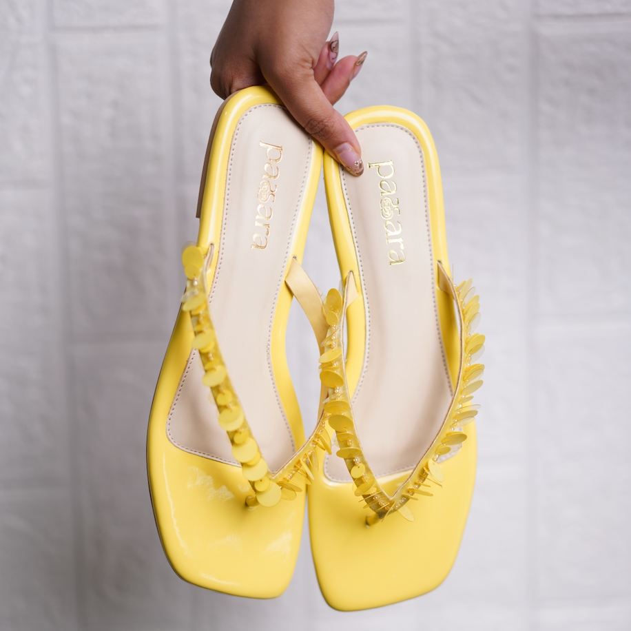 Yellow shoes with decorative straps held by a hand against a light gray background