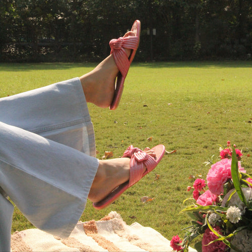 Person wearing pink sandals on a grassy area with flowers and trees in the background