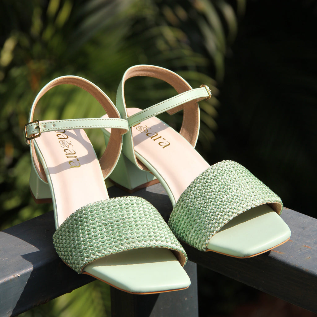 Green high-heeled shoes with thin straps on a blurred natural background