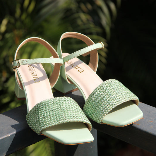 Green high-heeled shoes with thin straps on a blurred natural background