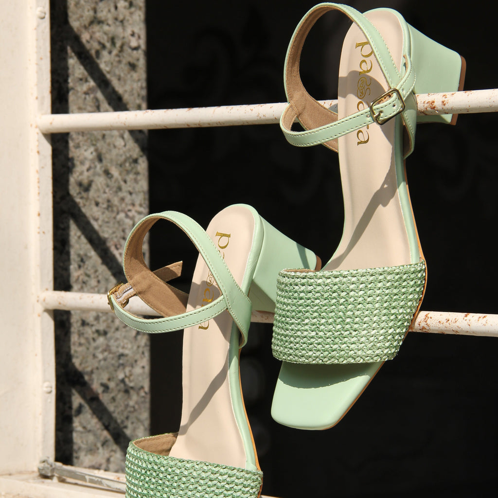 Pair of green high-heeled sandals with pearl straps on a metal surface.