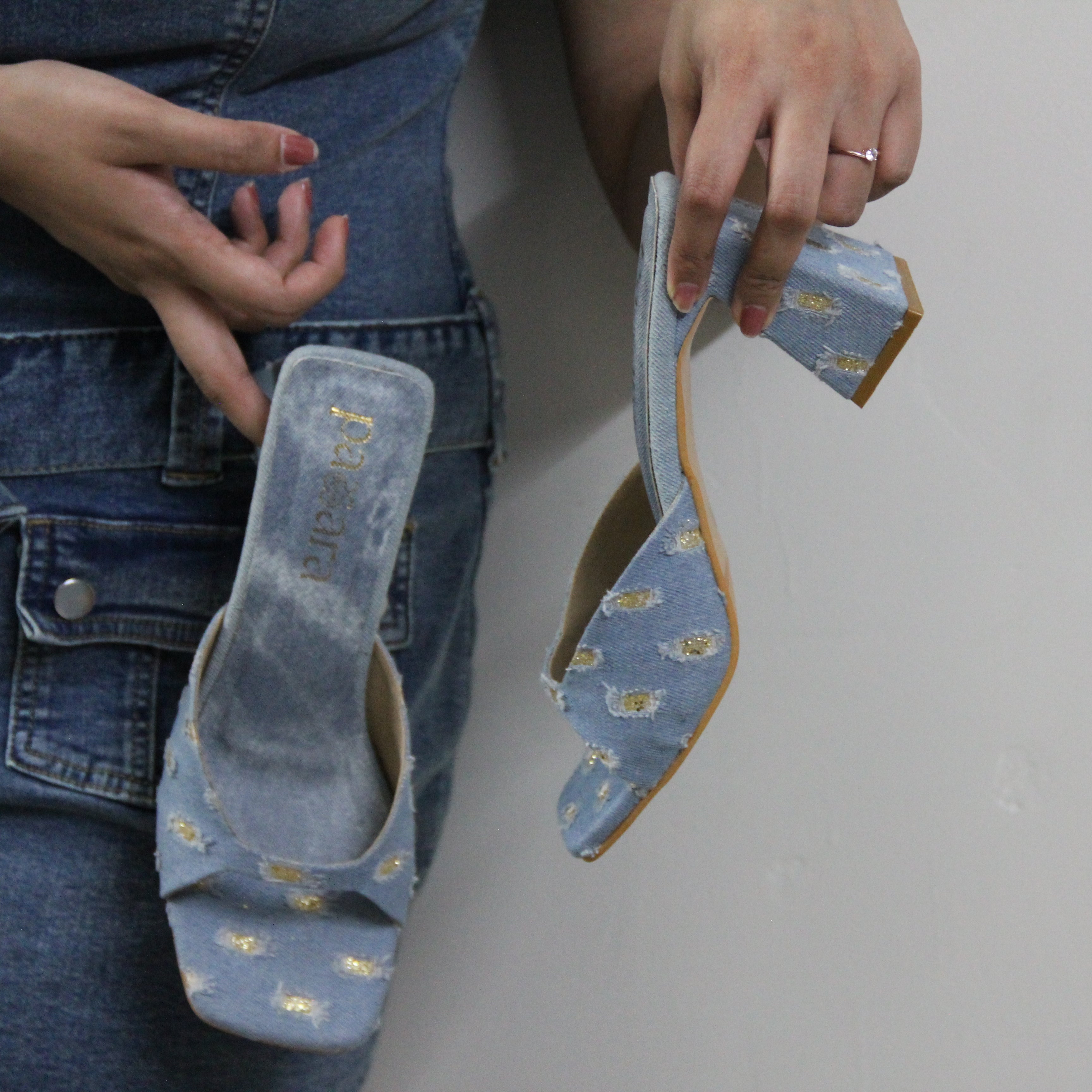 Person holding a pair of blue high-heeled shoes with a box on a plain background