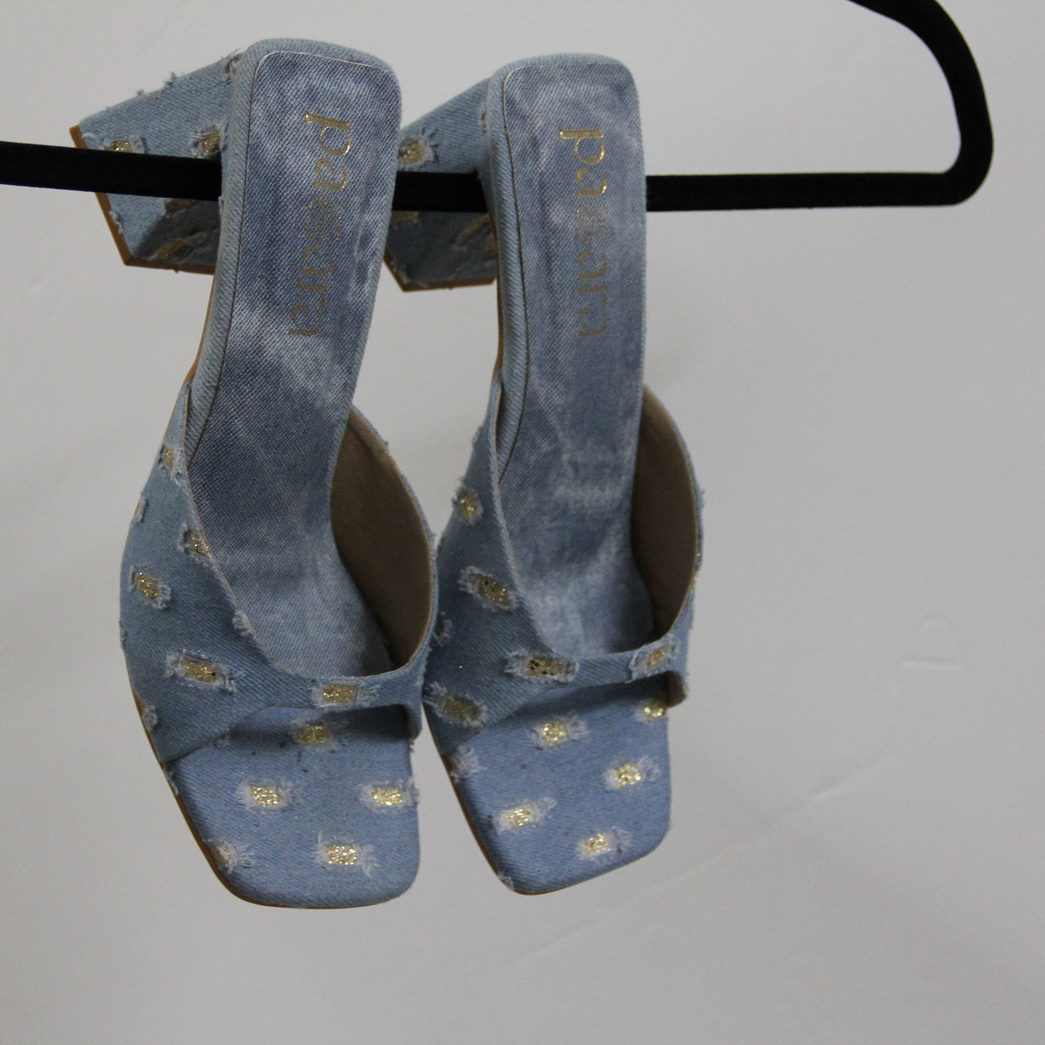 Pair of blue suede shoes with gold patterns on a black hanger against a gray background