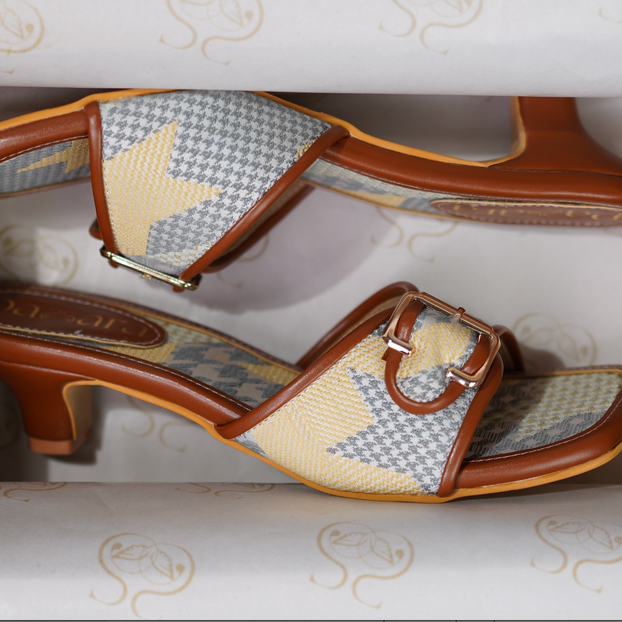 Pair of high-heeled shoes with patterned straps in a box
