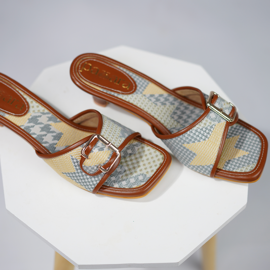 Pair of patterned sandals with brown straps on a white stand against a gray background