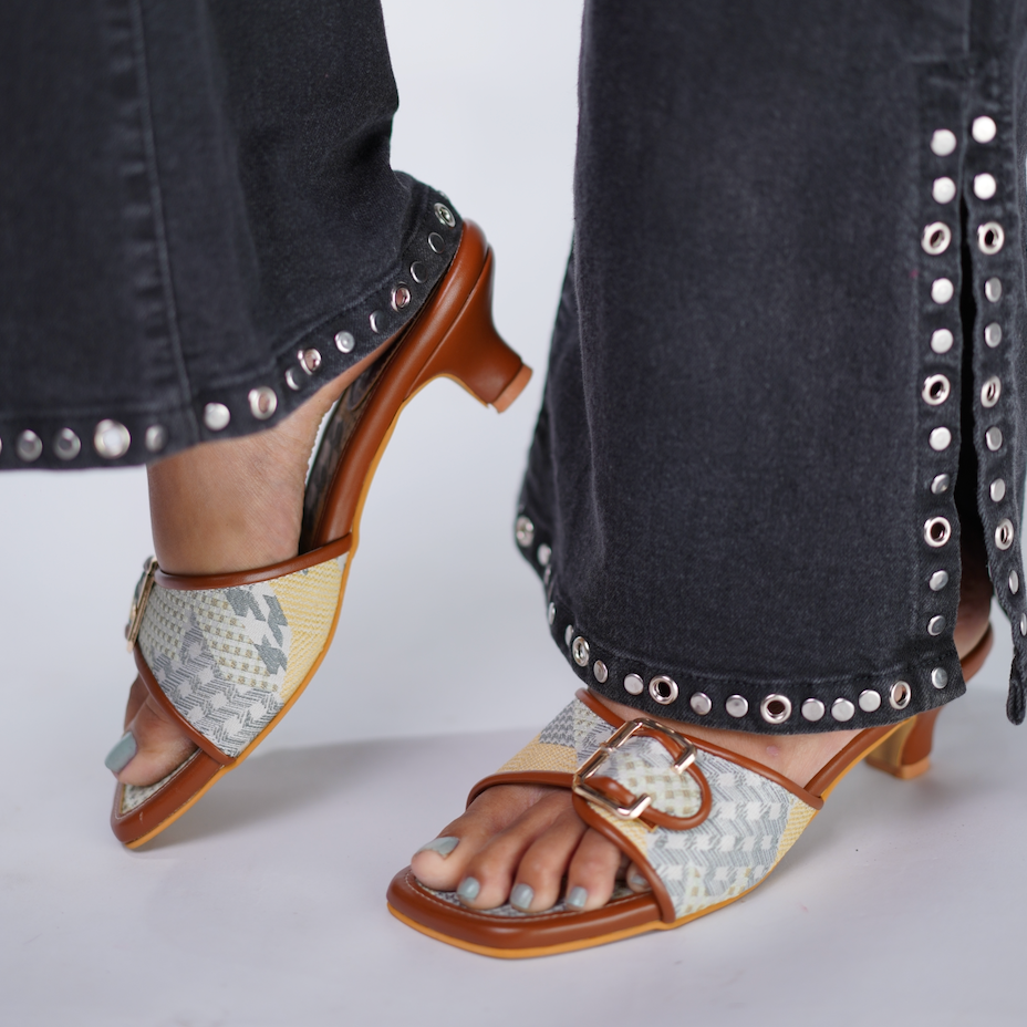 Close-up of feet wearing patterned sandals with a studded detail on jeans.