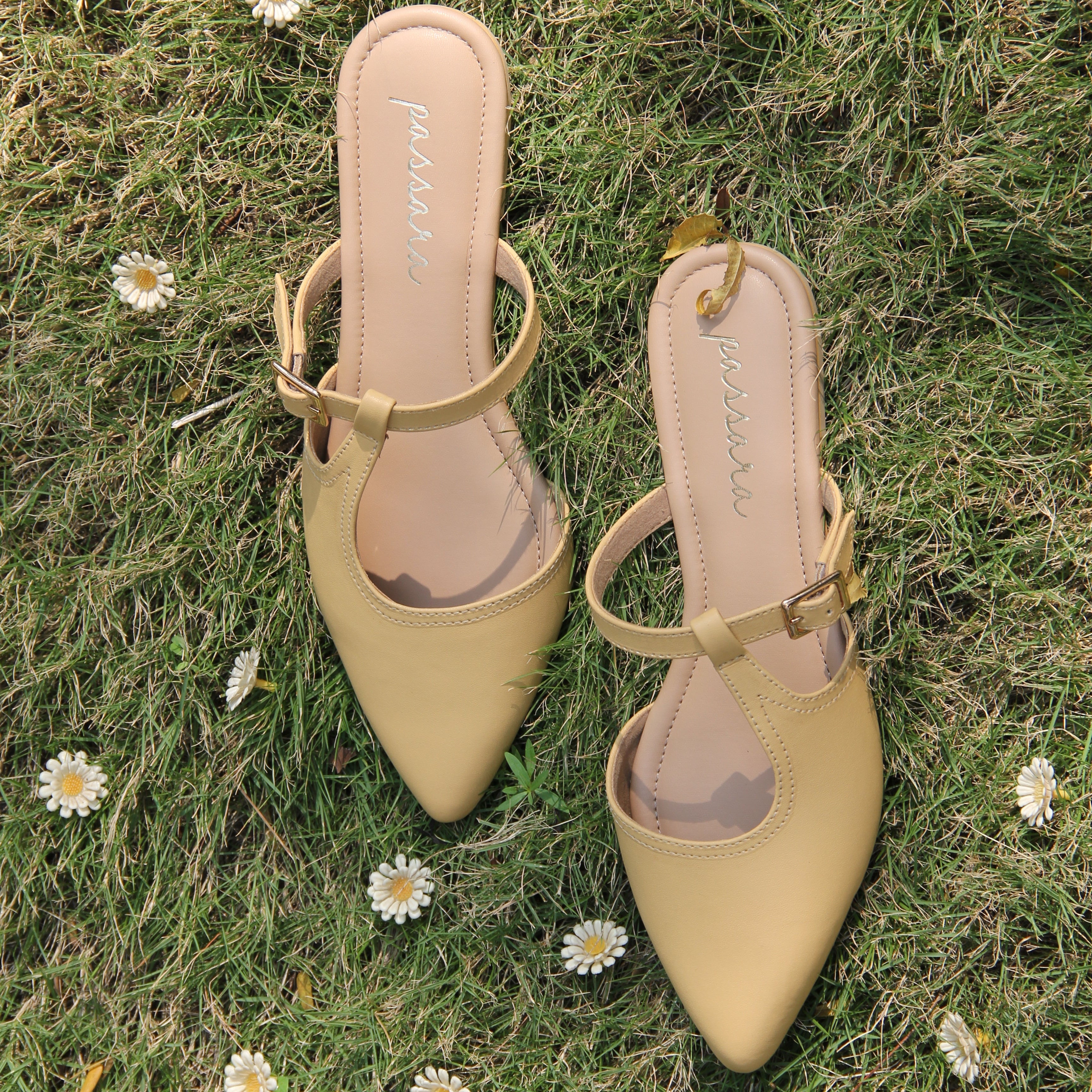 Pair of beige sandals on a grassy background with daisies