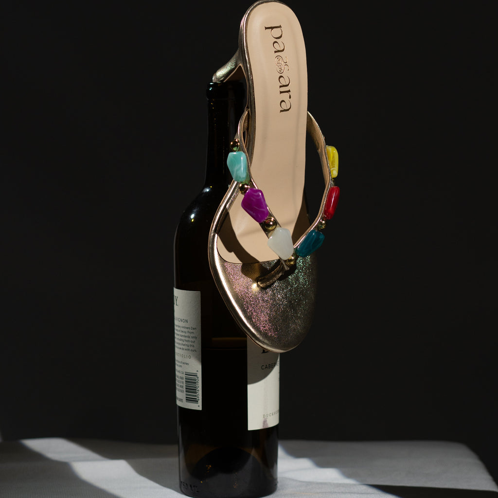 Multicolored sandal with gemstones on a bottle against a black background