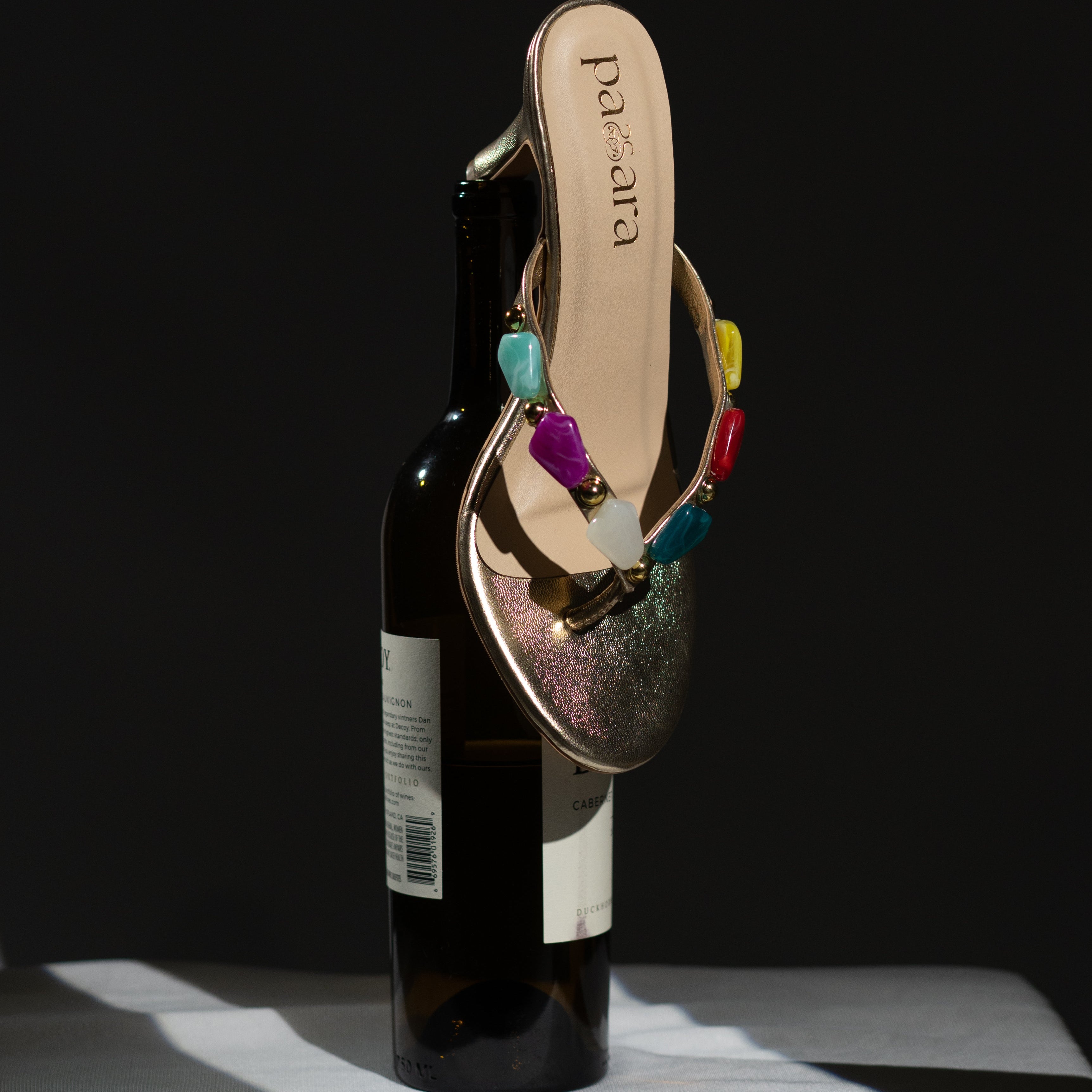Multicolored sandal with gemstones on a bottle against a black background